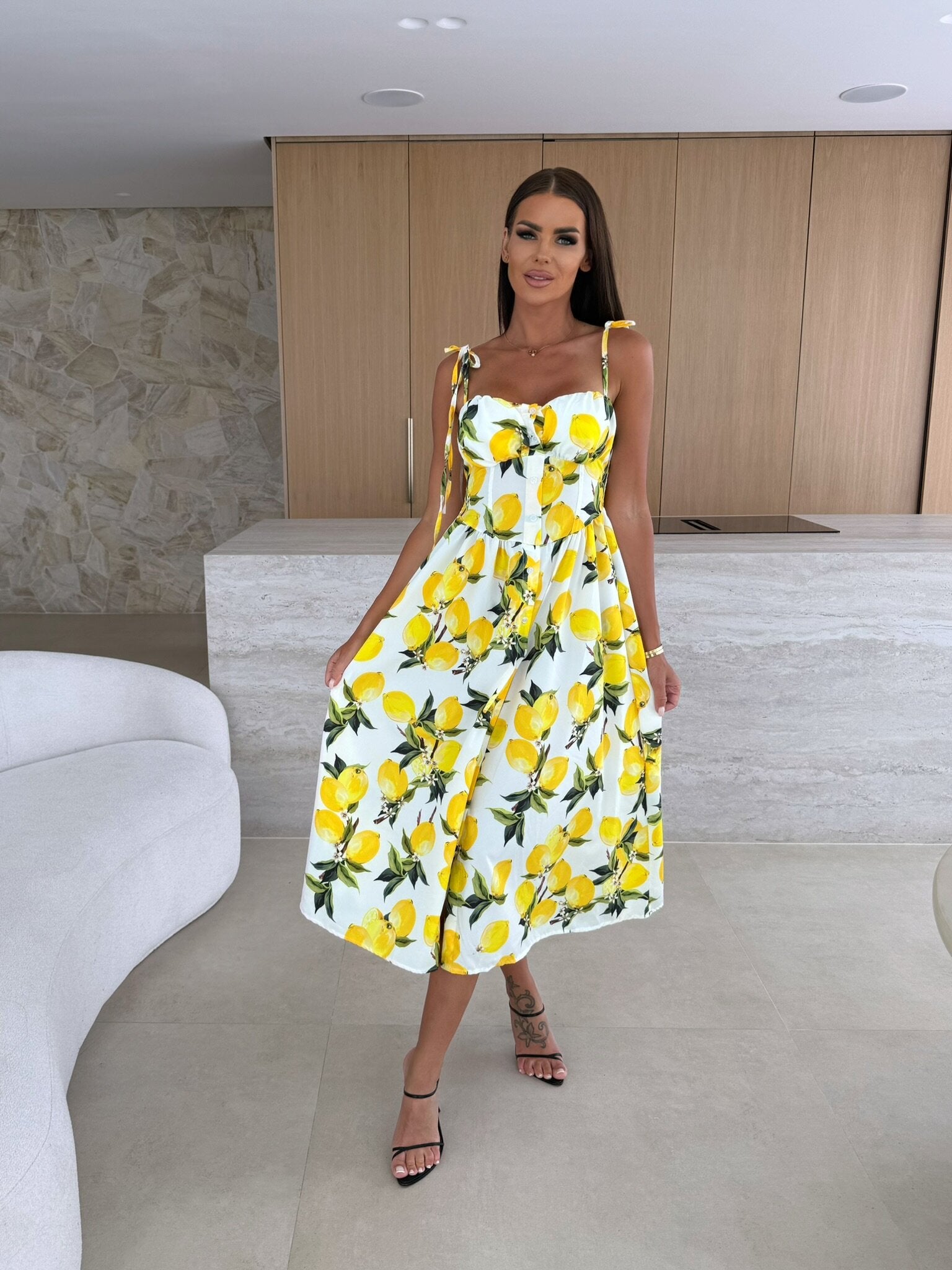 Woman wearing a yellow and white dress with lemon print in an indoor setting.