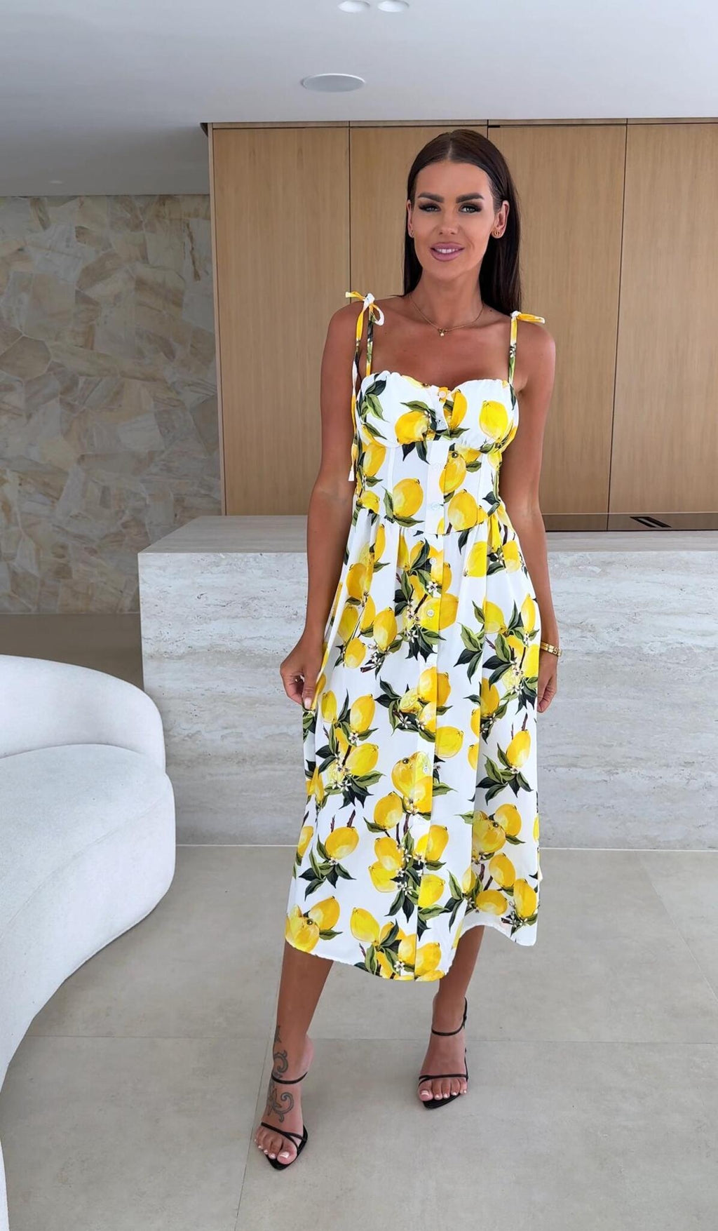 Woman wearing a white dress with yellow floral patterns in an indoor setting.