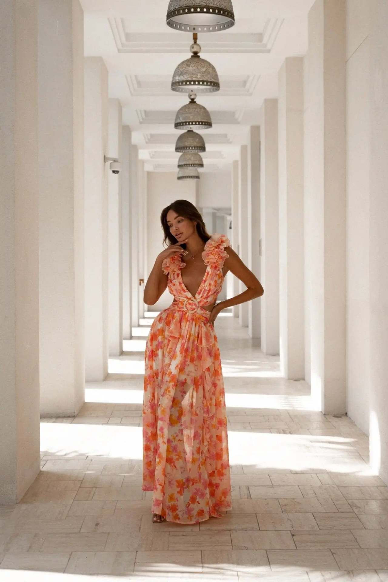 Woman in a floral dress standing in a sunlit hallway with columns