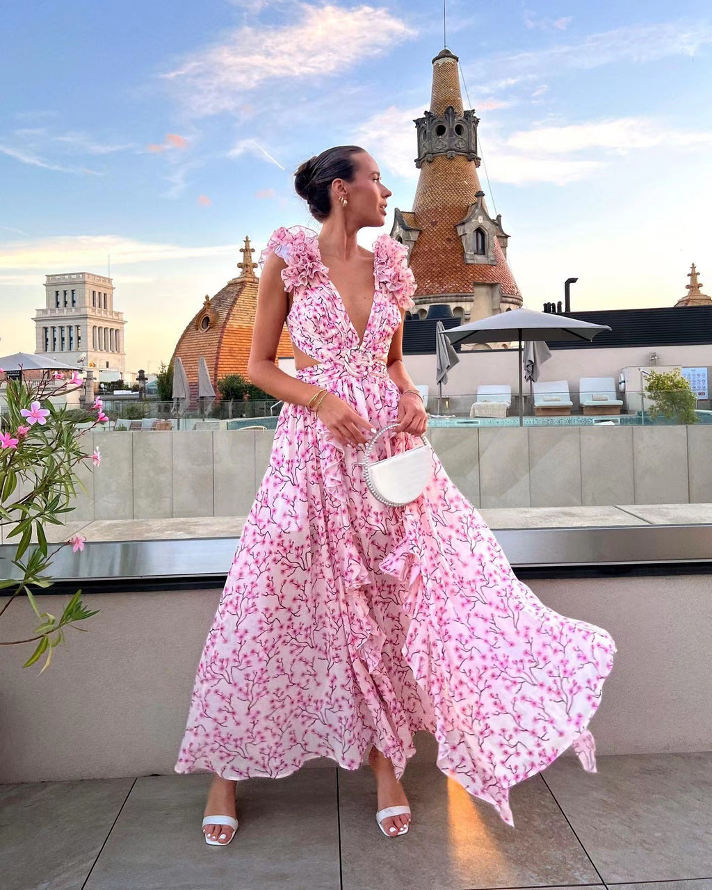 Woman in a pink floral dress standing on a rooftop with architectural landmarks in the background