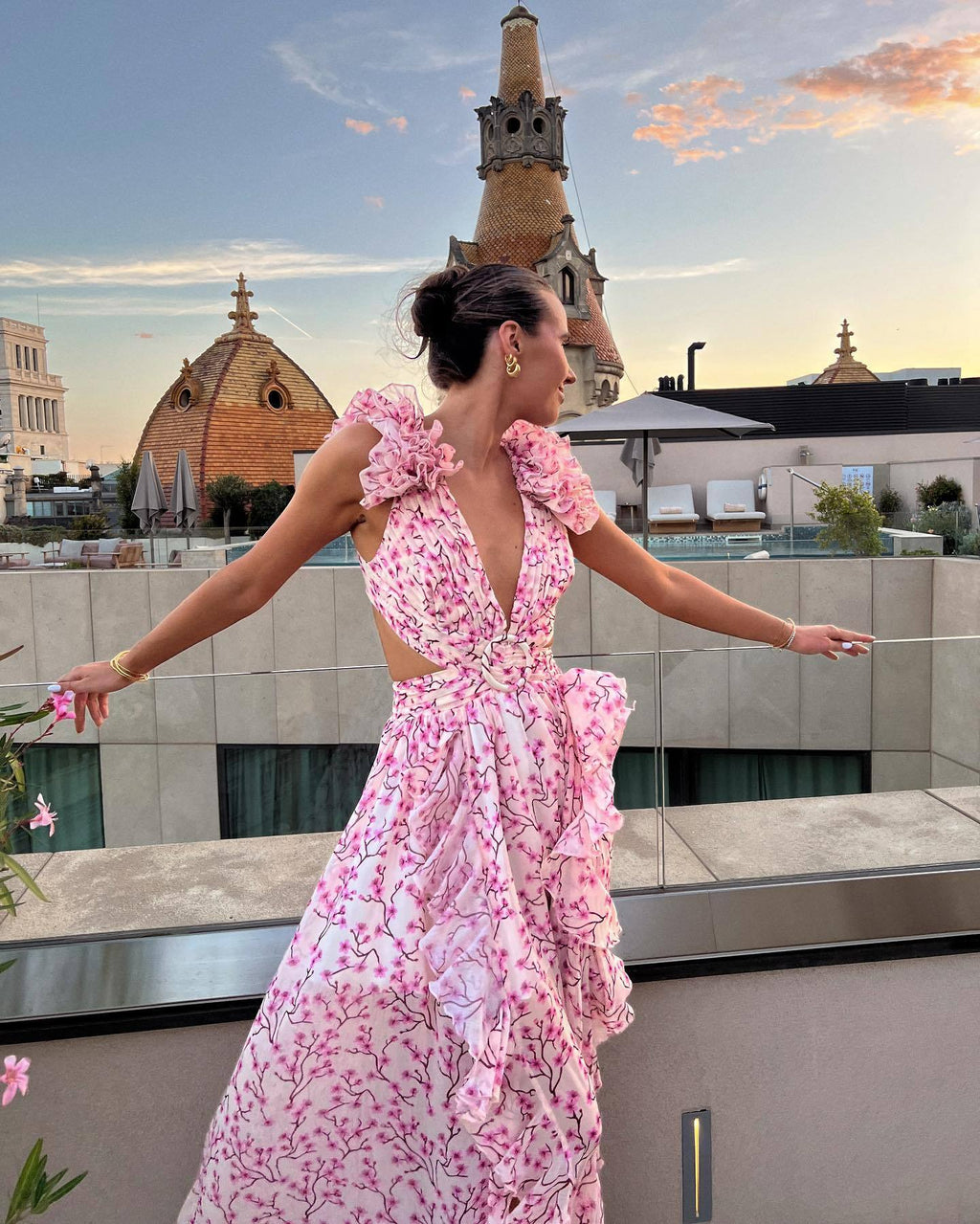 Woman in a pink floral dress on a rooftop with a cityscape background