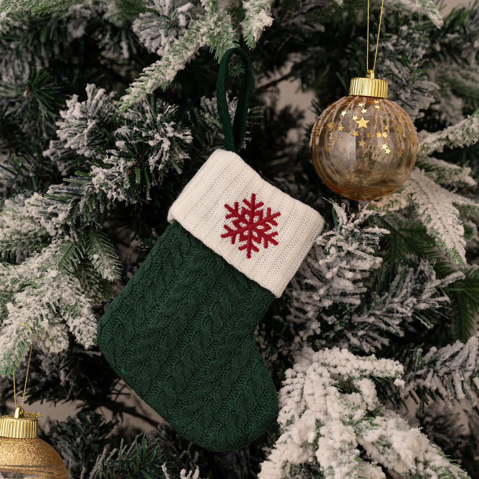 Green knitted Christmas stocking with a red snowflake design hanging on a decorated tree.