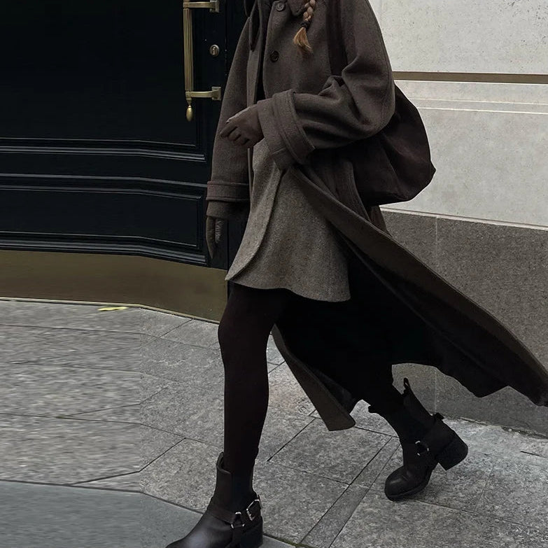 Person wearing a long coat and black boots on a city street.