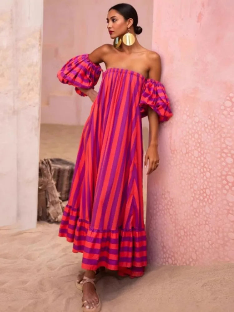 Woman wearing a colorful striped dress against a pink wall.