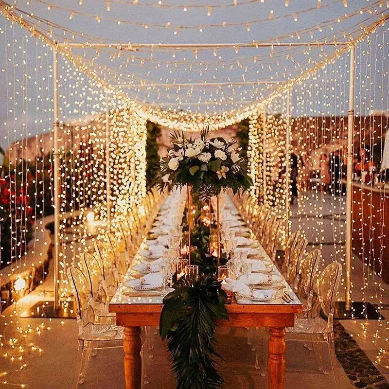 Decorated outdoor table with string lights and floral arrangements.