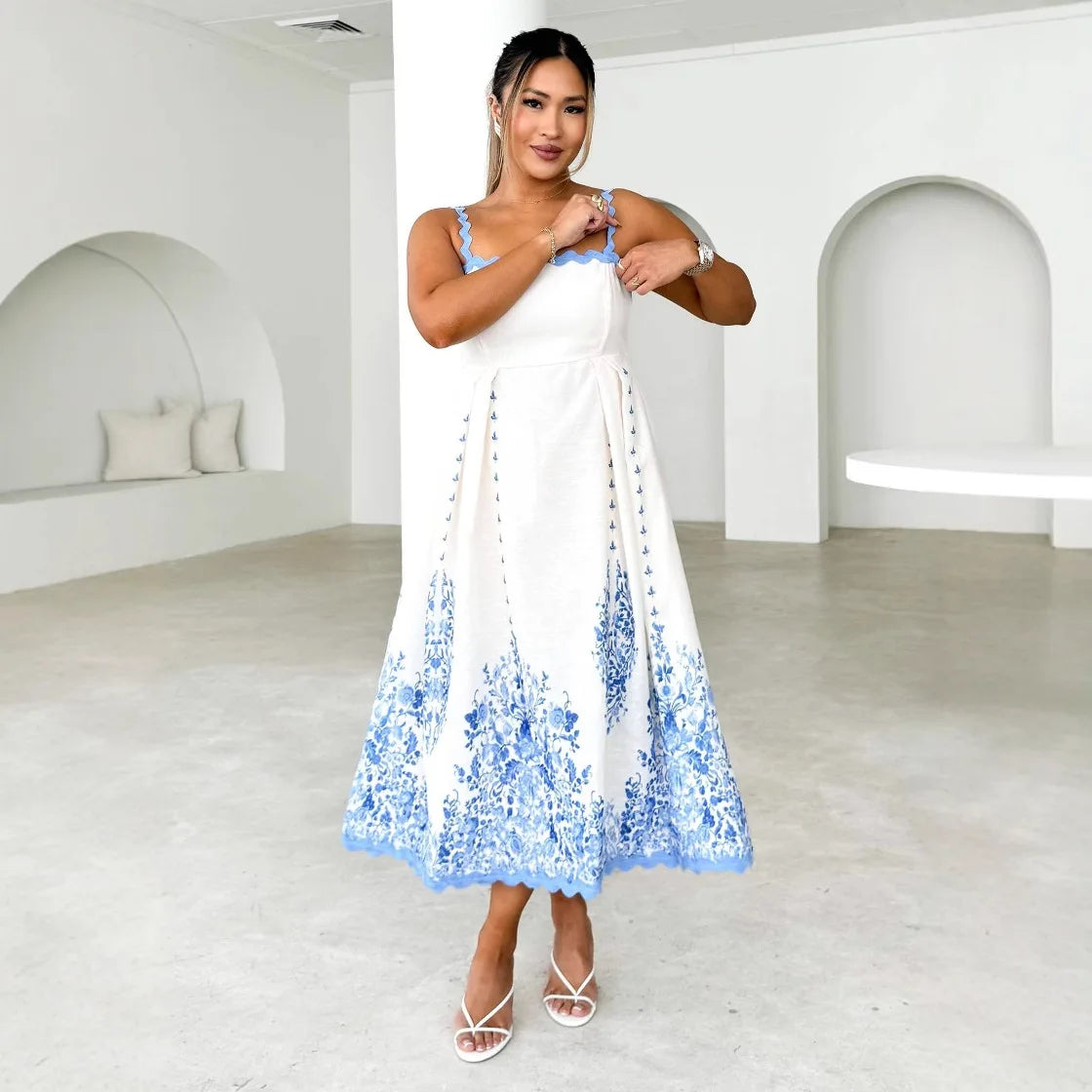 Woman wearing a white dress with blue floral patterns in a minimalistic room.