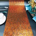 Shiny orange and gold table runner on a black table with silverware and plates.