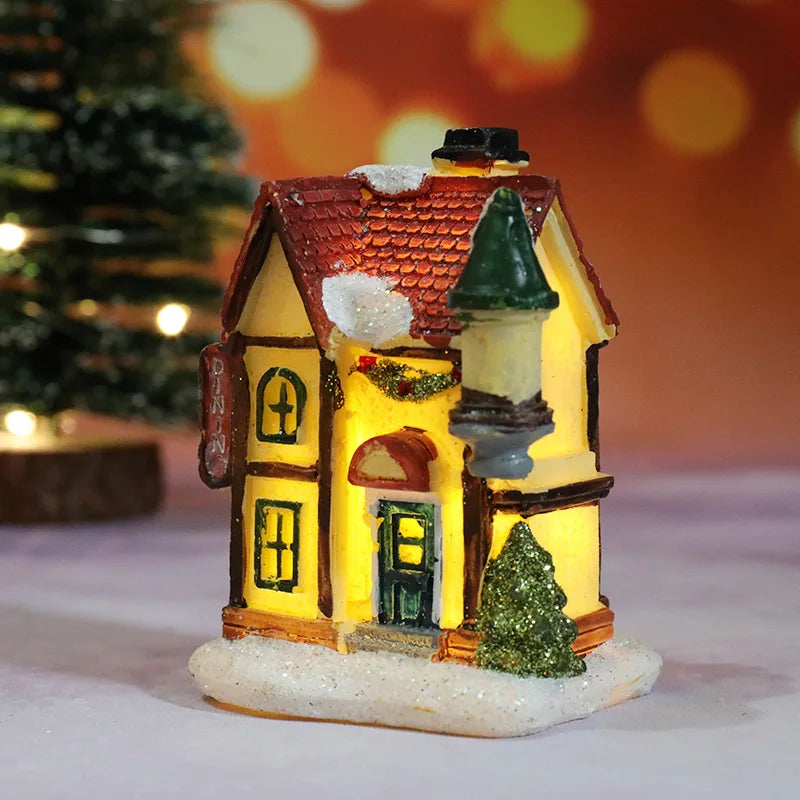 Decorative miniature house with a lit interior, surrounded by festive decorations on a blurred background.