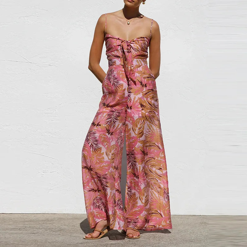Woman wearing a pink floral jumpsuit against a white wall.