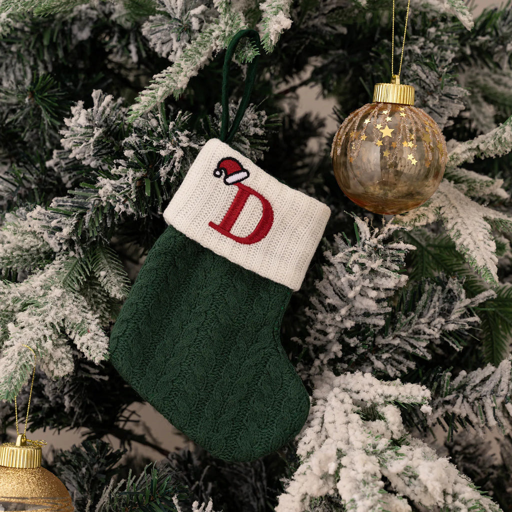Green Christmas stocking with red letter 'D' and white cuff hanging on a decorated tree.