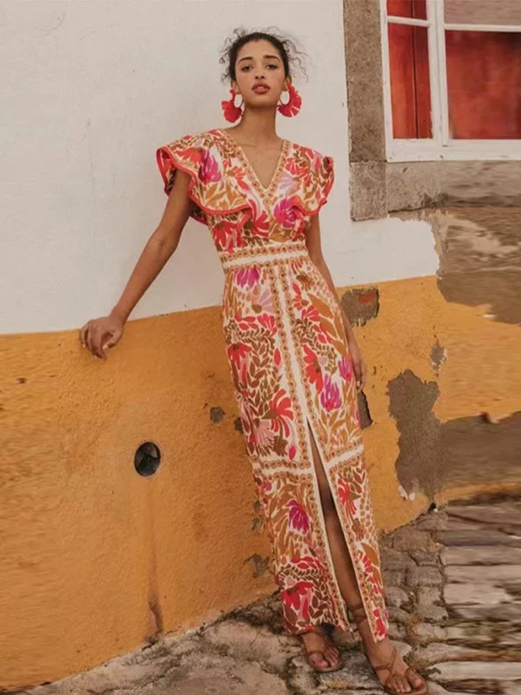 Woman in a floral dress standing against a rustic wall.
