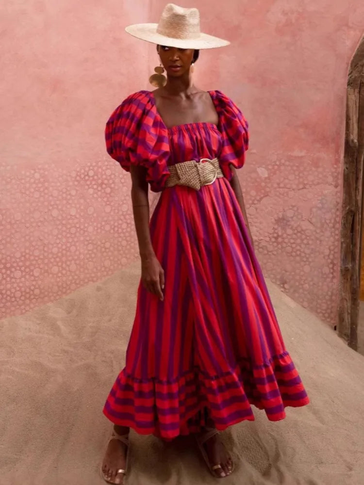 Woman wearing a red and purple striped dress with puffed sleeves against a pink textured wall.