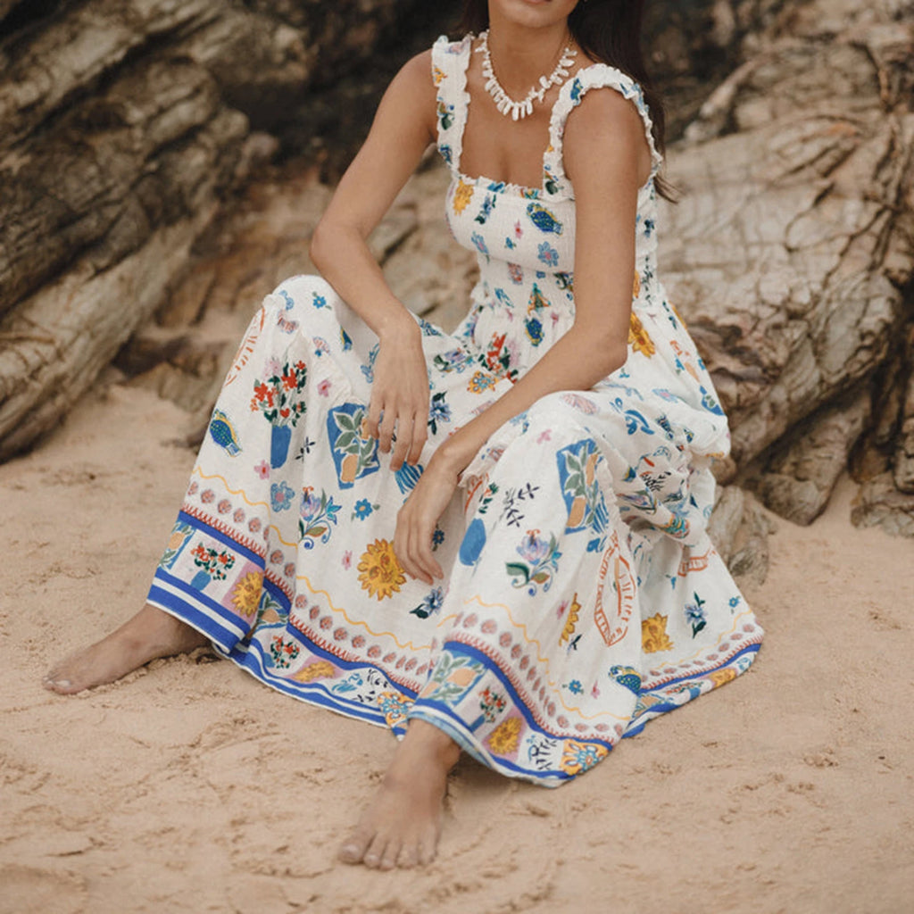 Woman in a floral dress sitting on a sandy beach with large rocks in the background