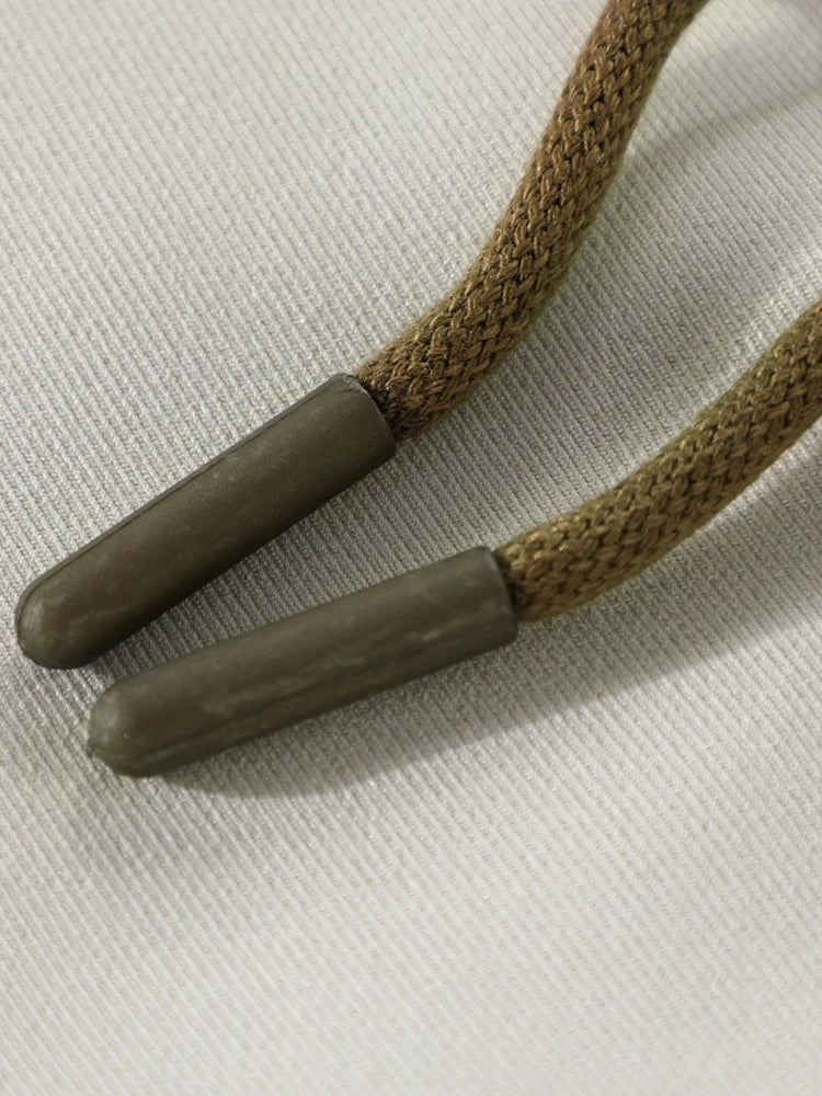 Close-up of a braided cord with two brown leather ends on a light beige background