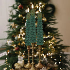 Decorative teal Christmas tree candles on gold stands with a blurred Christmas tree in the background.