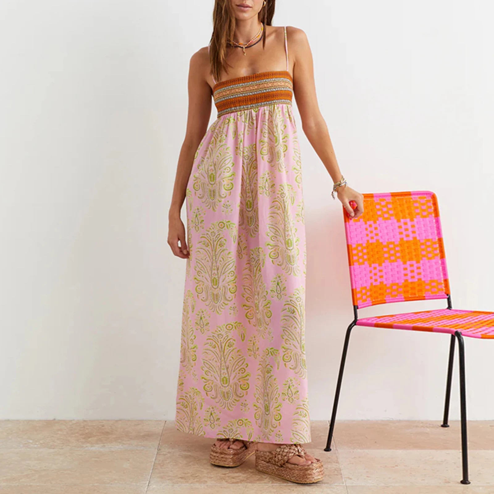 Woman in a pink dress standing next to a colorful chair against a white wall.