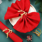 Red napkin with gold reindeer holder on a green surface with Christmas decorations.