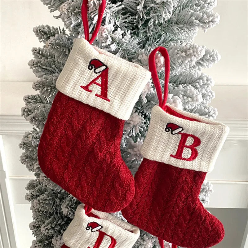 Red Christmas stockings with white cuffs and red lettering hanging on a decorated tree.
