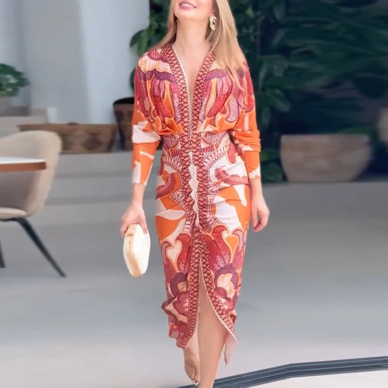 Woman in an orange and red patterned dress standing indoors with a blurred background