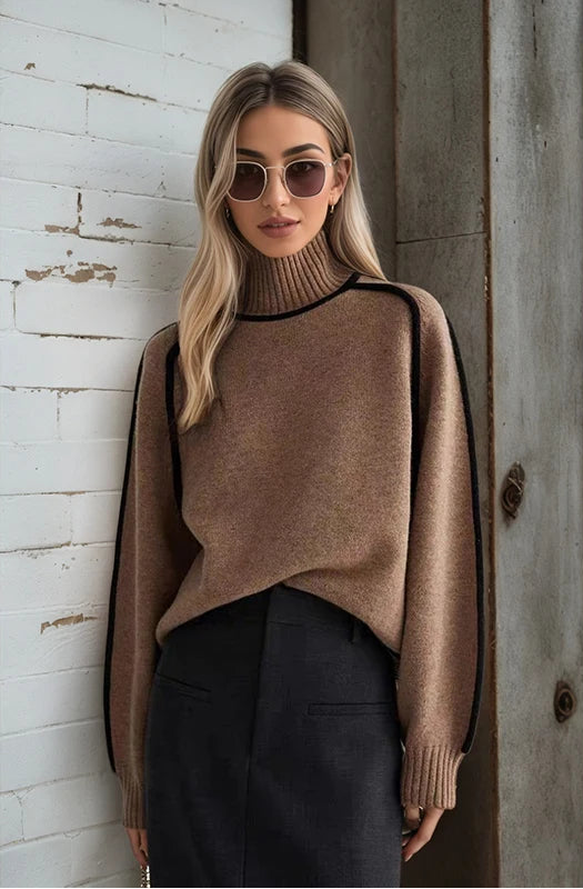 Woman wearing a brown sweater and sunglasses against a textured wall.