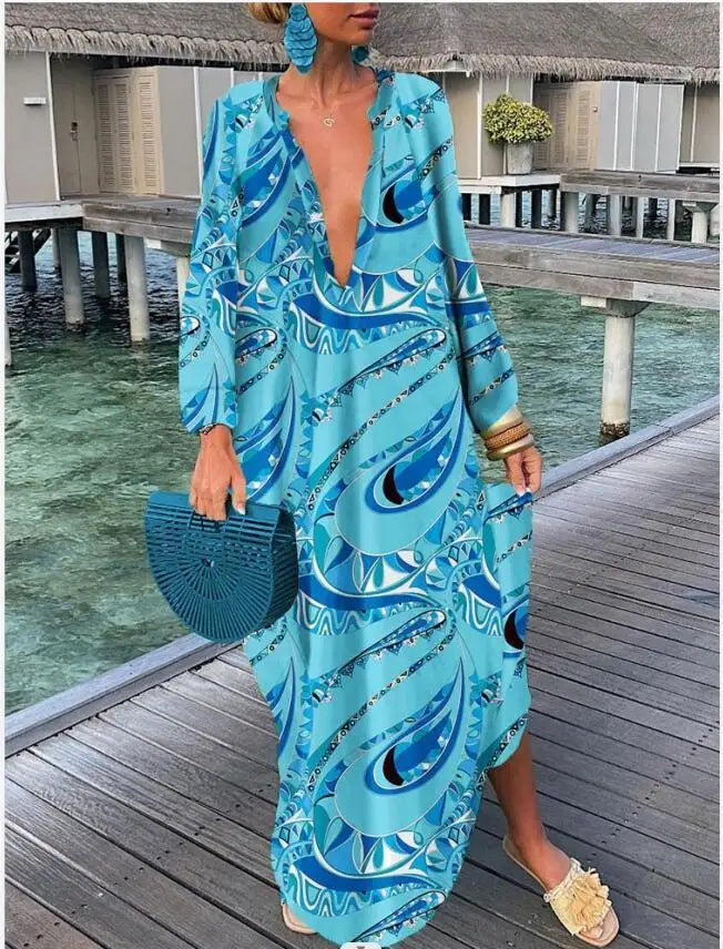 Woman in a blue patterned dress standing on a wooden dock by water.