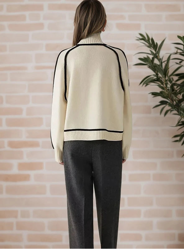 Person wearing a cream sweater with black accents against a brick wall.