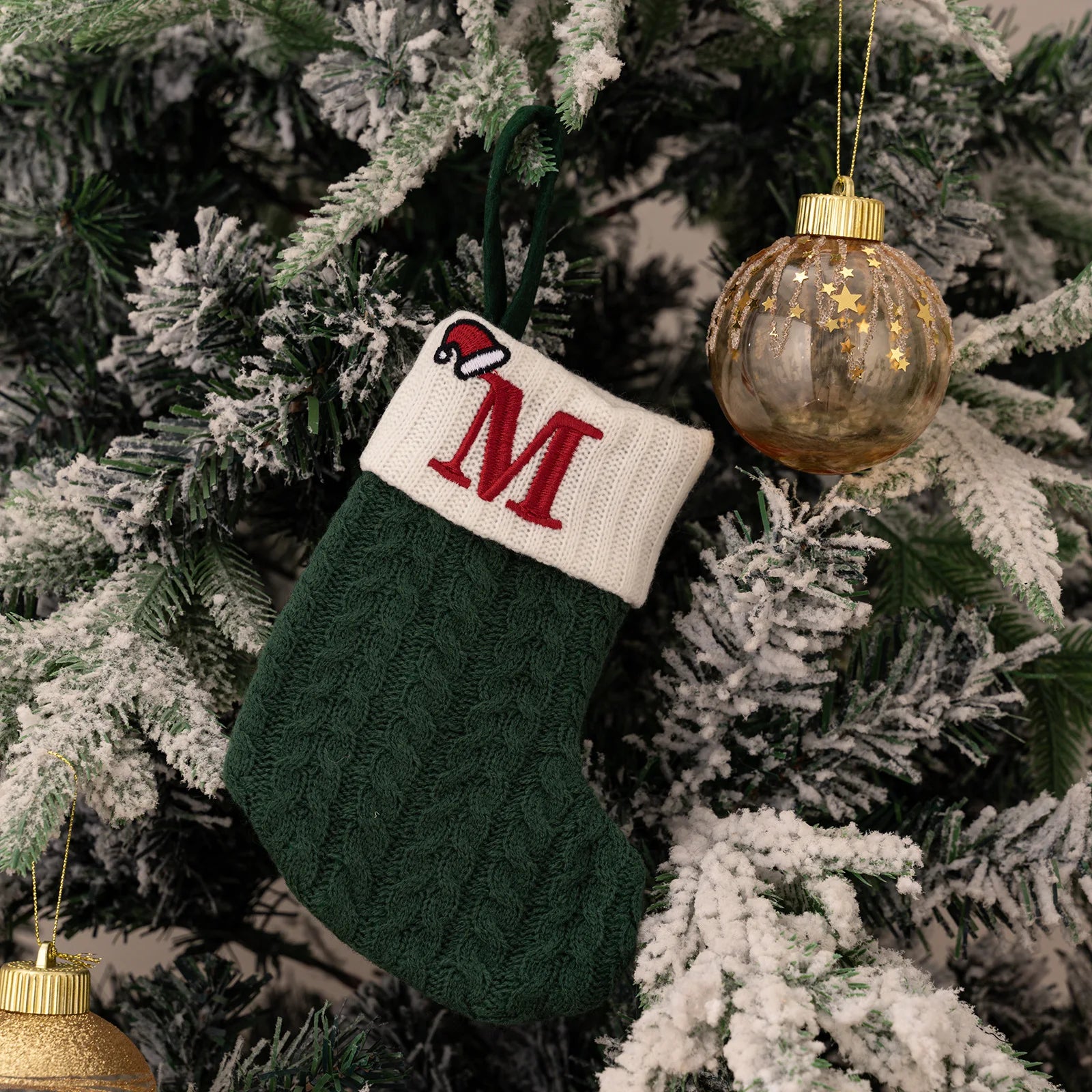 Green Christmas stocking with red letter 'M' hanging on a decorated tree.