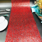 Red glittery table runner on a black surface with silverware and a decorative item.