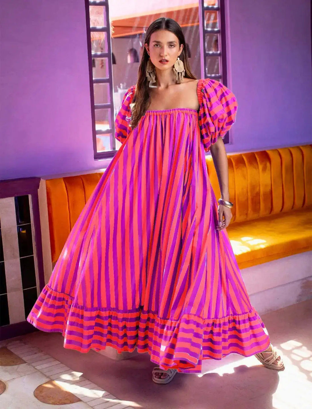 Woman wearing a vibrant pink and purple striped dress in a colorful room.