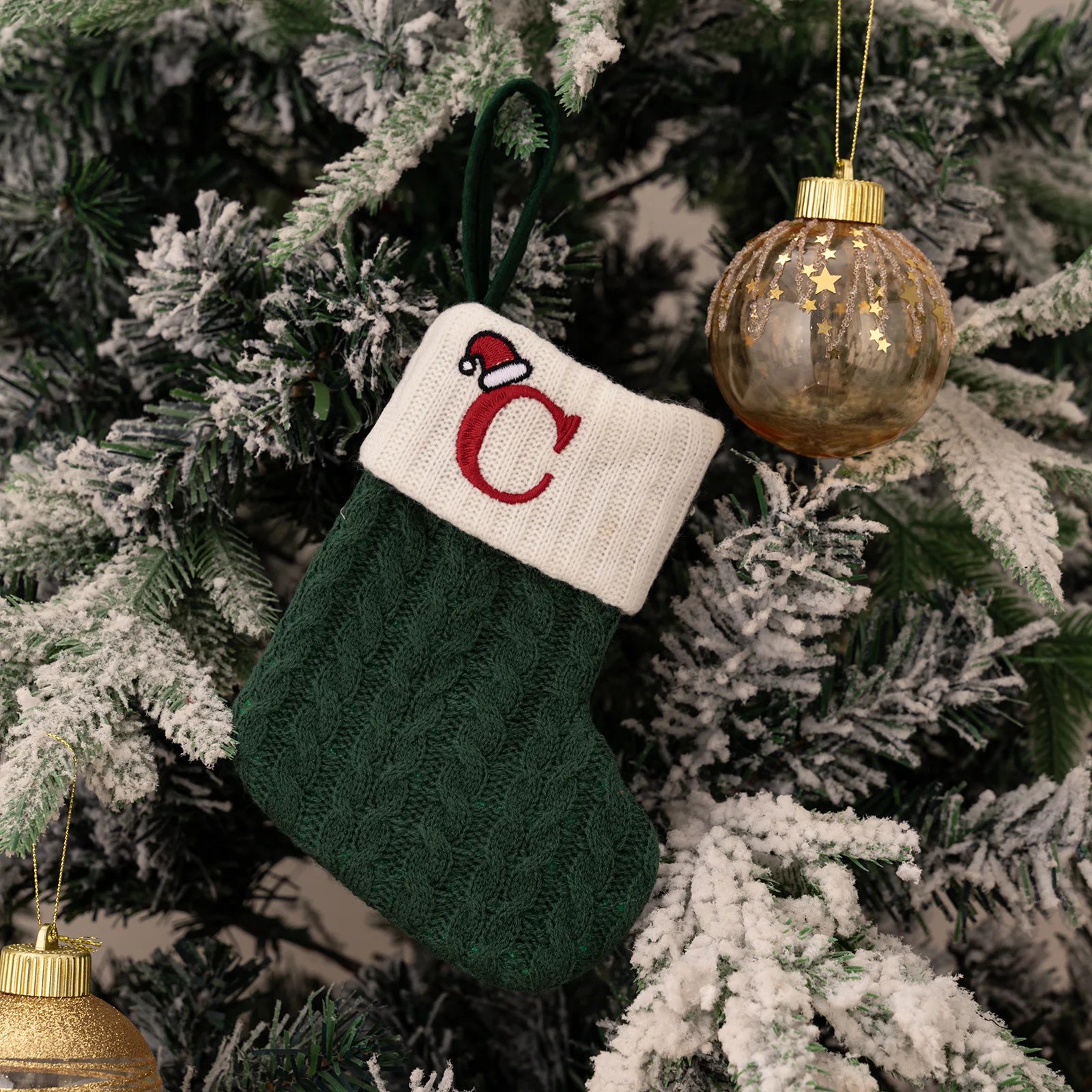 Green knitted Christmas stocking with a red letter 'C' on a decorated tree.