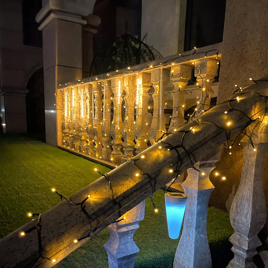 Decorative string lights on a stone railing and wall with a building in the background.