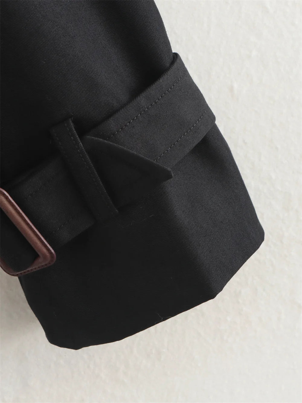 Close-up of a black coat with a belt on a textured white background