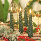 Decorative Christmas tree candles on a festive table setting with lights and greenery.