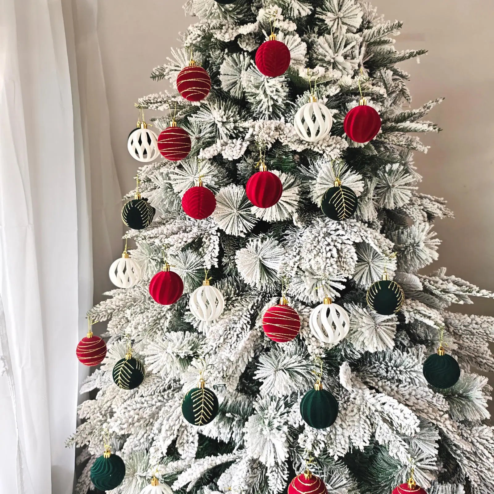 Decorated Christmas tree with red, white, and green ornaments against a neutral wall.