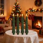 Set of five green Christmas tree-shaped candles on a table with a decorated living room in the background.
