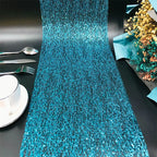 Turquoise sequin table runner on a black table with silverware and a cup.