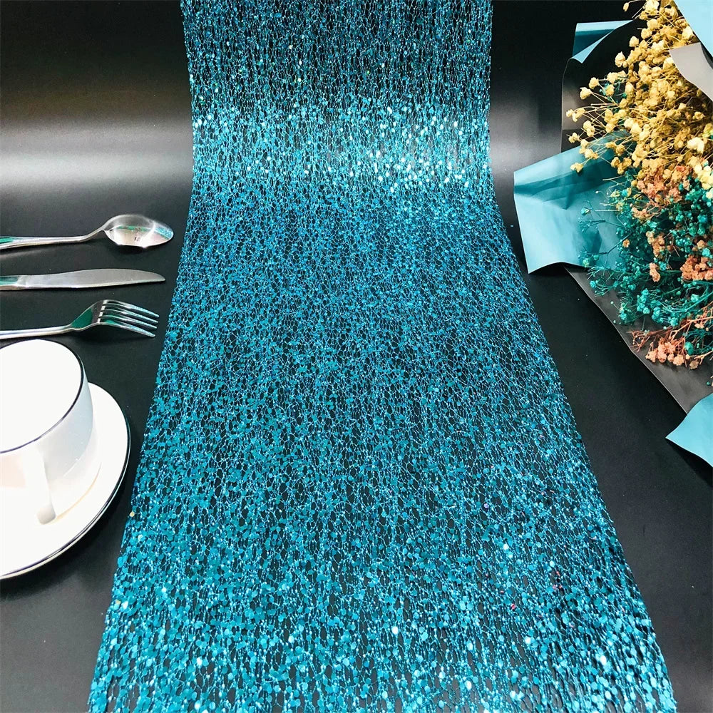 Turquoise sequin table runner on a black table with silverware and a cup.