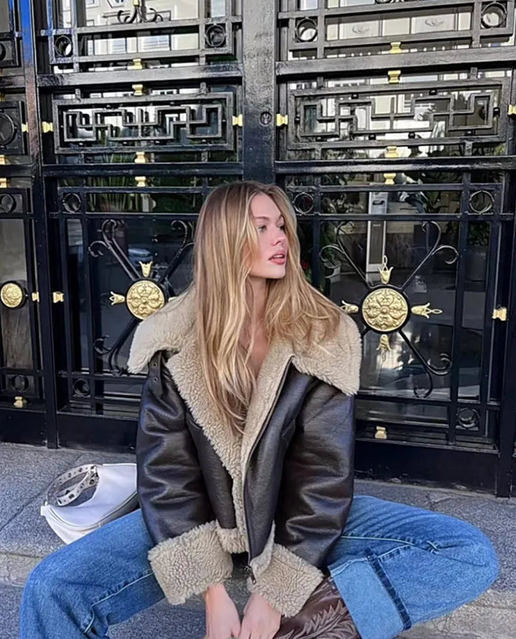 Woman wearing a leather jacket with fur lining sitting in front of a large metal gate.