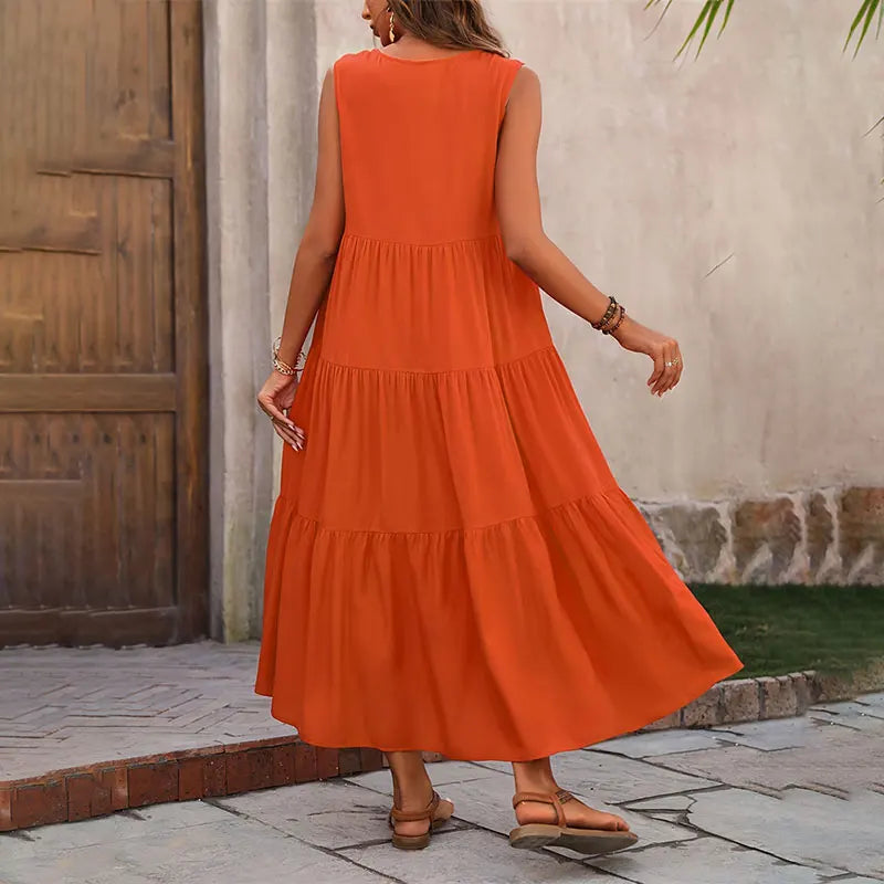 Woman wearing an orange dress standing on a stone path with a rustic wall in the background
