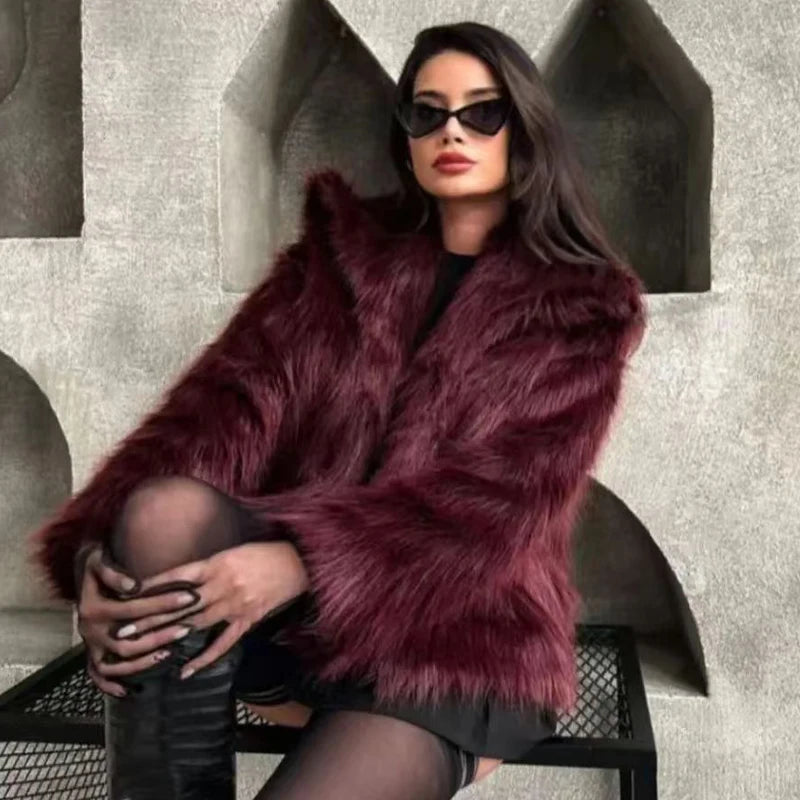 Woman wearing a burgundy fur coat and sunglasses sitting on a chair.