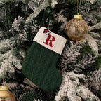 Green knitted Christmas stocking with a red letter 'R' on a decorated tree.