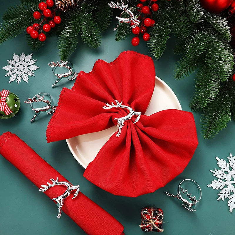 Red napkin with silver reindeer clip on a white plate, surrounded by Christmas decorations on a green background.