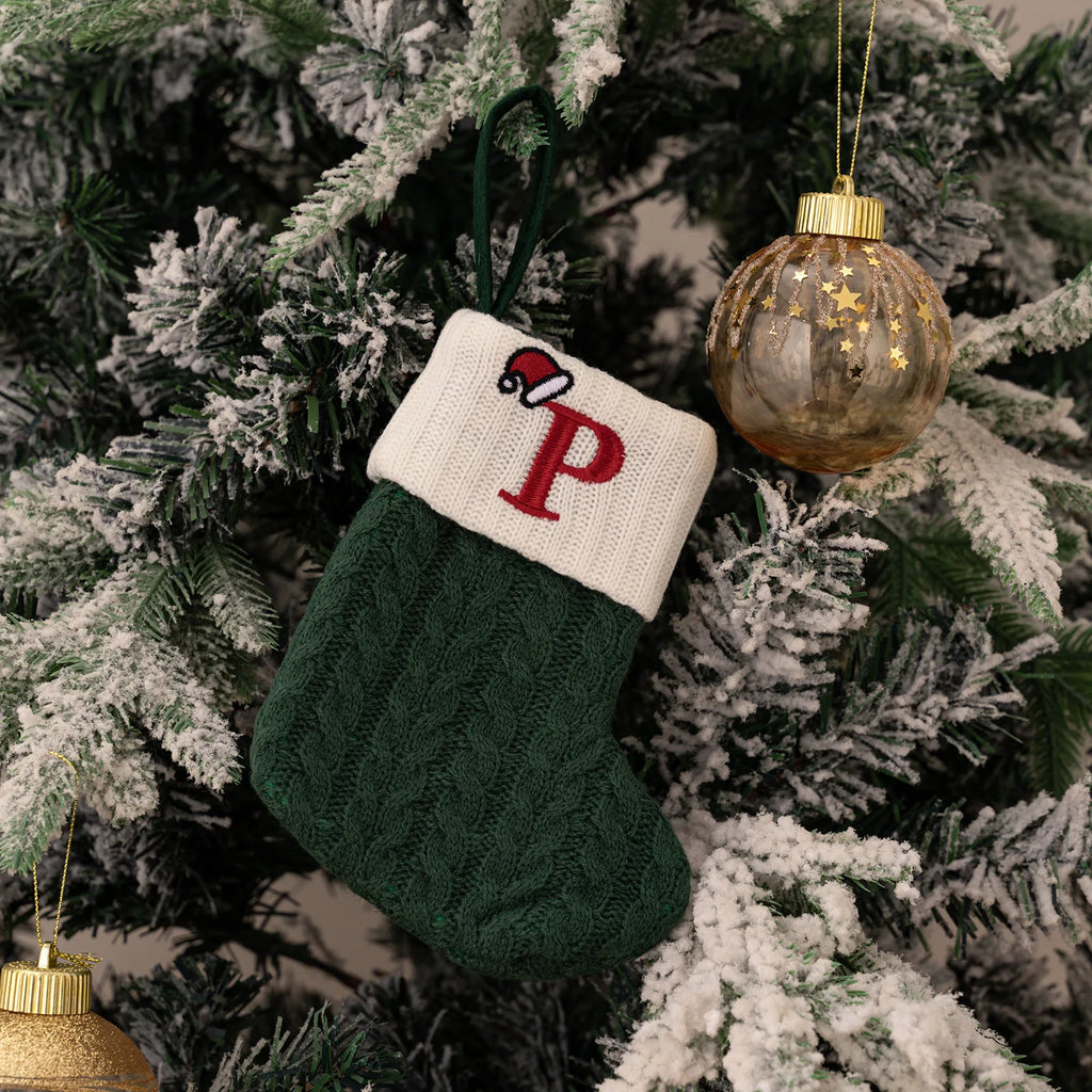 Green and white Christmas stocking with a red letter 'P' hanging on a decorated tree.