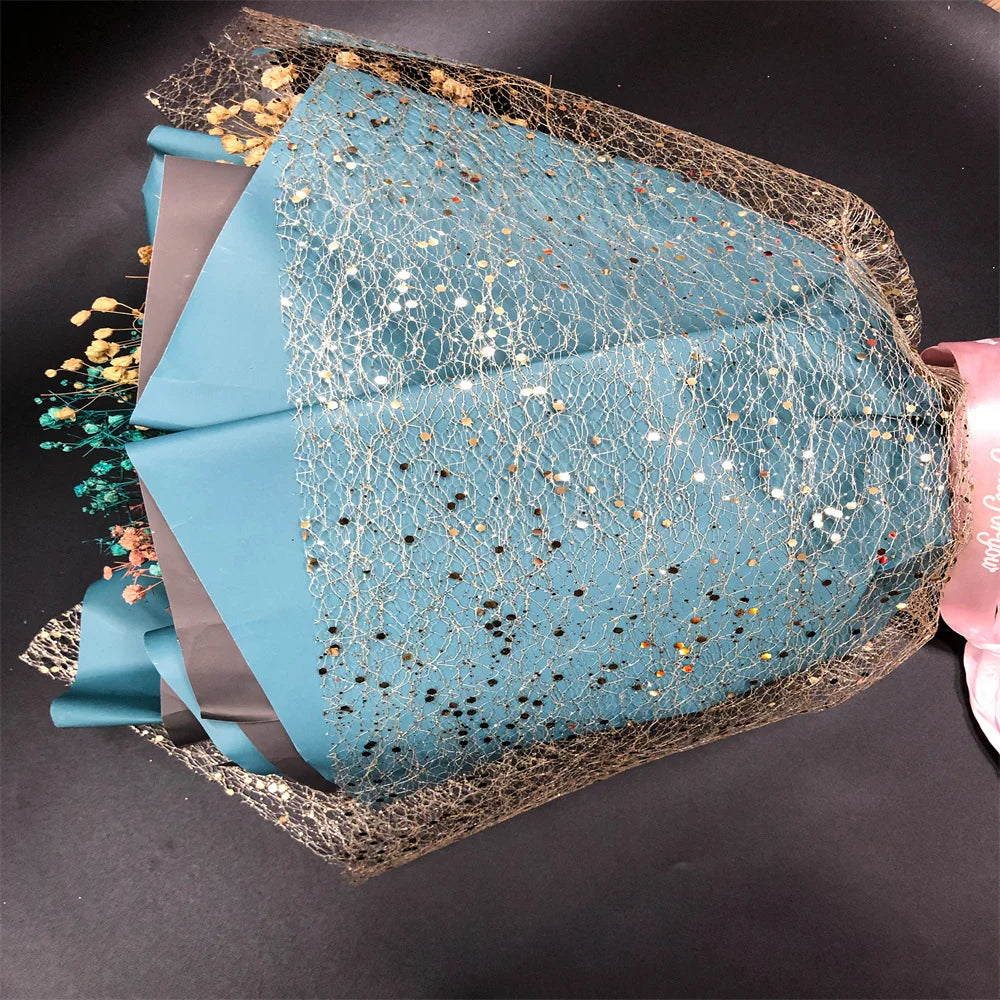 Bouquet wrapped in blue paper with gold and silver confetti on a dark background