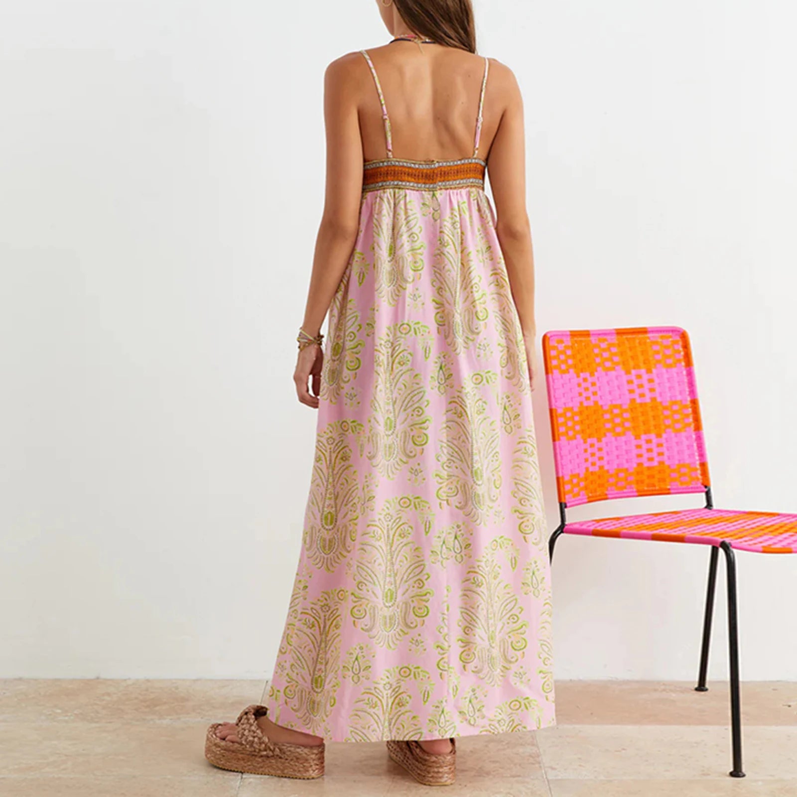 Woman wearing a pink floral dress standing next to a colorful chair on a wooden floor.