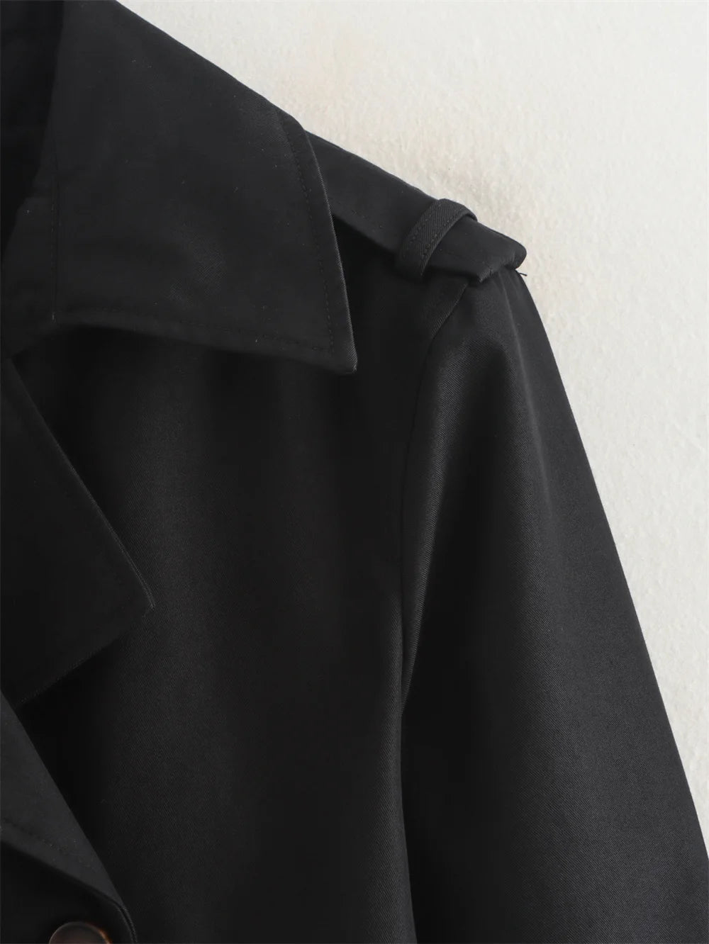 Close-up of a black coat with a belt on a light background