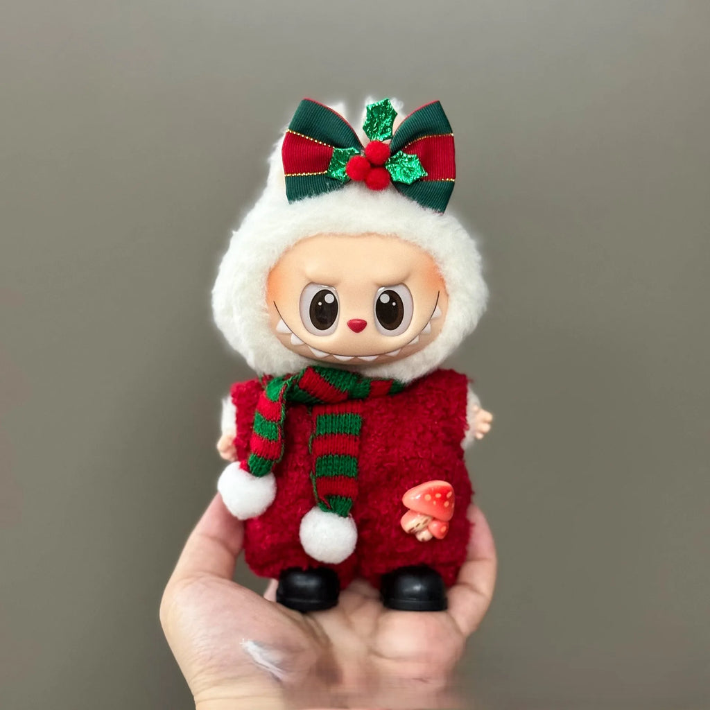 Small doll in a red and green outfit with a white hood, held against a gray background.