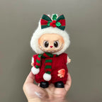 Small doll in a red and green outfit with a white hood, held against a gray background.
