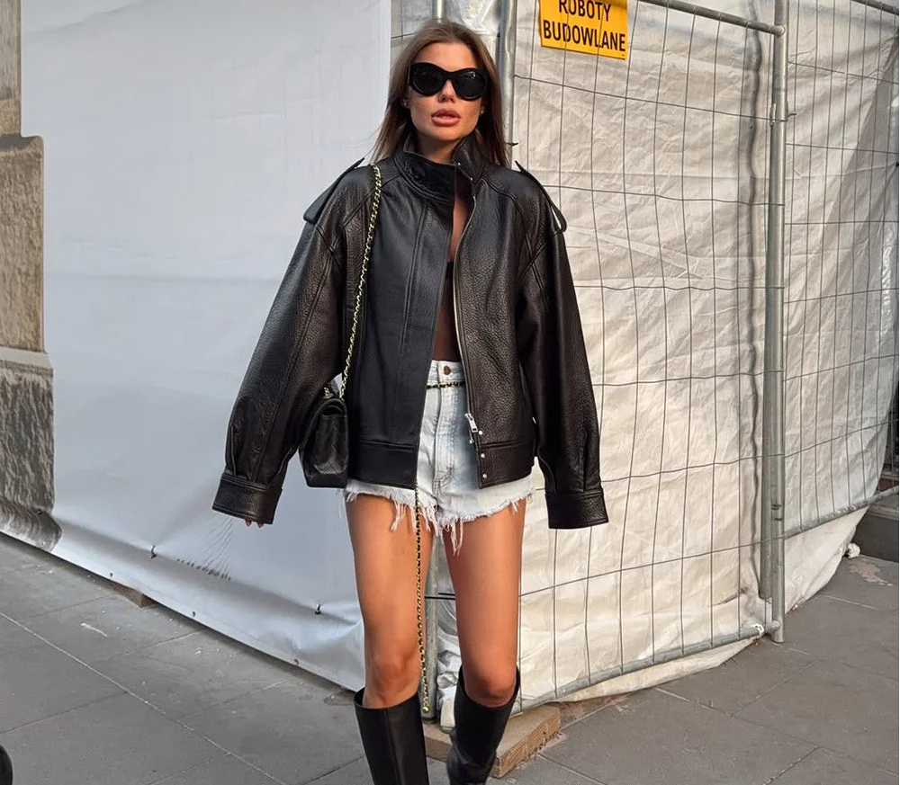 Woman wearing a black leather jacket and sunglasses, standing in front of a white wall with 'KONDALA' branding.