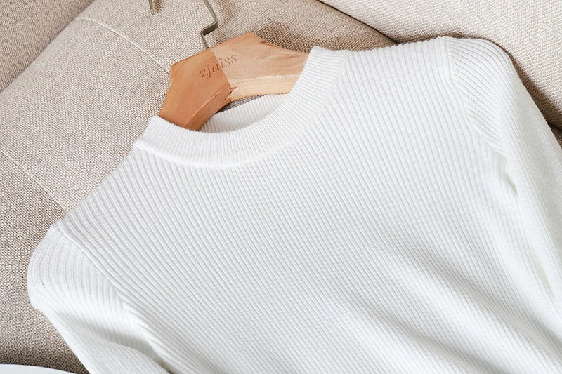 White sweater on a wooden hanger against a beige fabric background